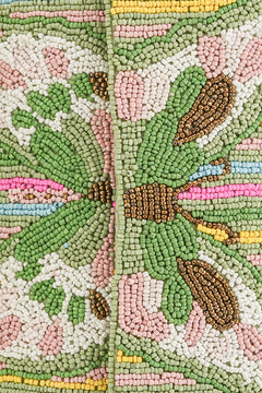 Close-up of a beaded fabric with leaf patterns in green, pink, and brown.