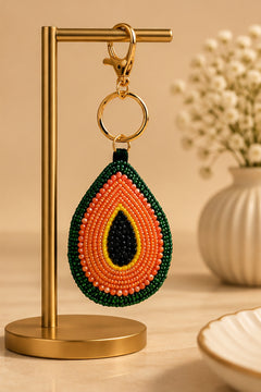 Orange, green and black beaded avocado keychain hanging on a gold stand