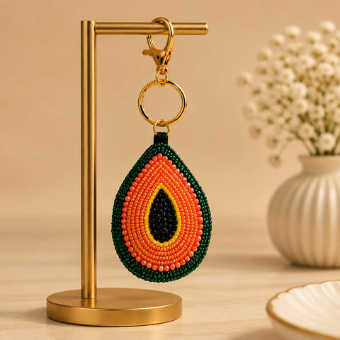 Orange, green and black beaded avocado keychain hanging on a gold stand