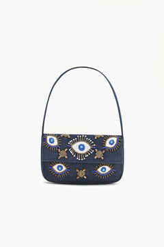 A dark blue denim shoulder bag with a single strap, decorated with embroidered evil eye motifs in blue.