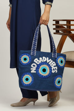 Person holding a blue tote bag with 'No Bad Vibes' text and eye designs.
