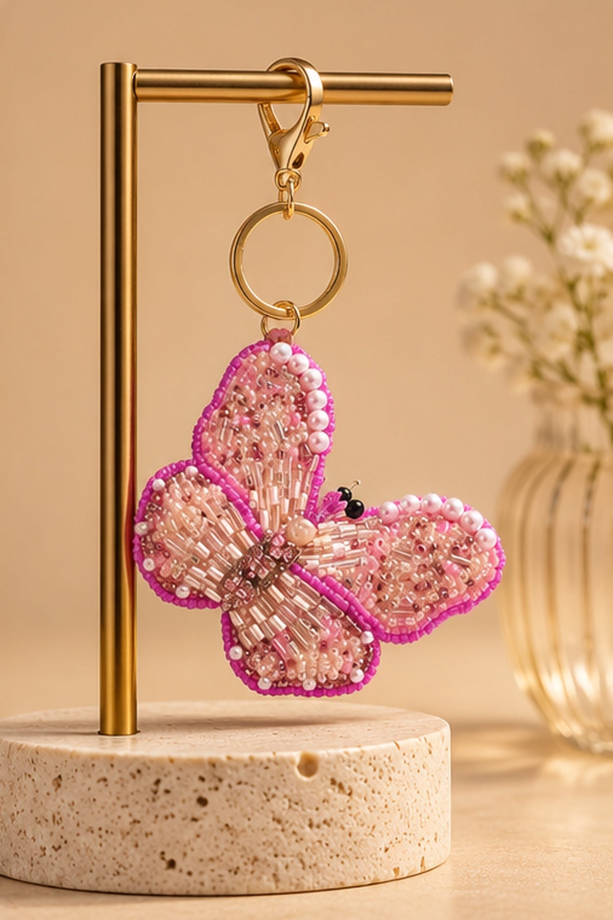 Pink beaded butterfly keychain with pearl accents hanging on a gold stand