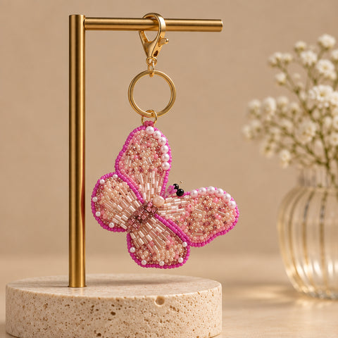 Pink beaded butterfly keychain with pearl accents hanging on a gold stand