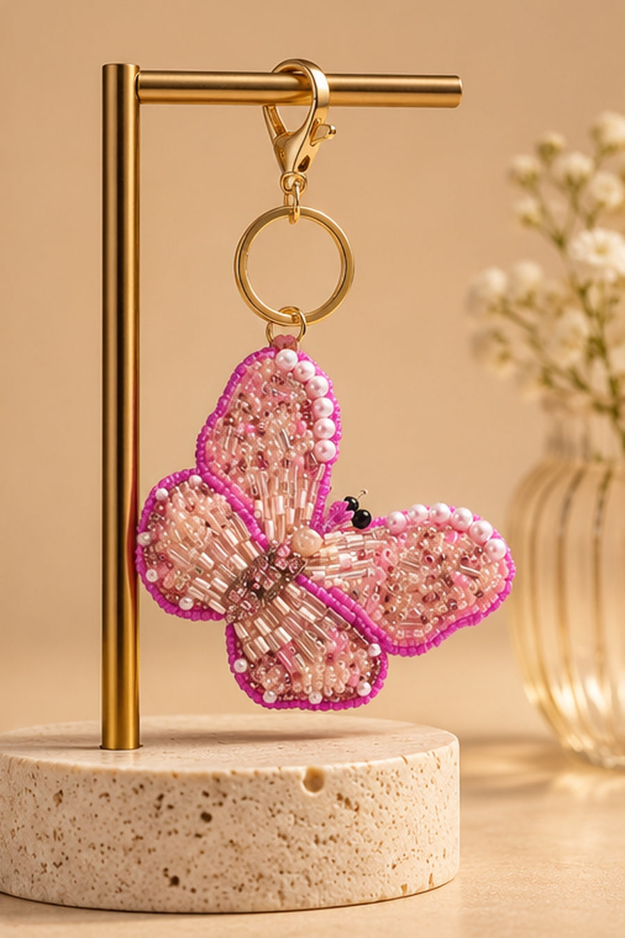 Pink beaded butterfly keychain with pearl accents hanging on a gold stand