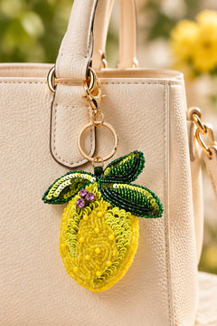 Yellow beaded lemon keychain with green sequin leaves on a stone tray